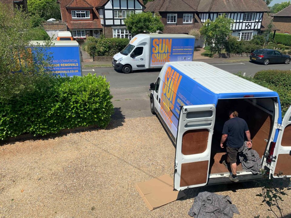 View from a house window, looking outside at three Sunshine Removals vans in the driveway and street.