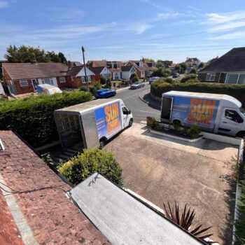 A street view from a first floor window showing two Sunshine Removals delivery vans parked in a driveway, surrounded by houses.